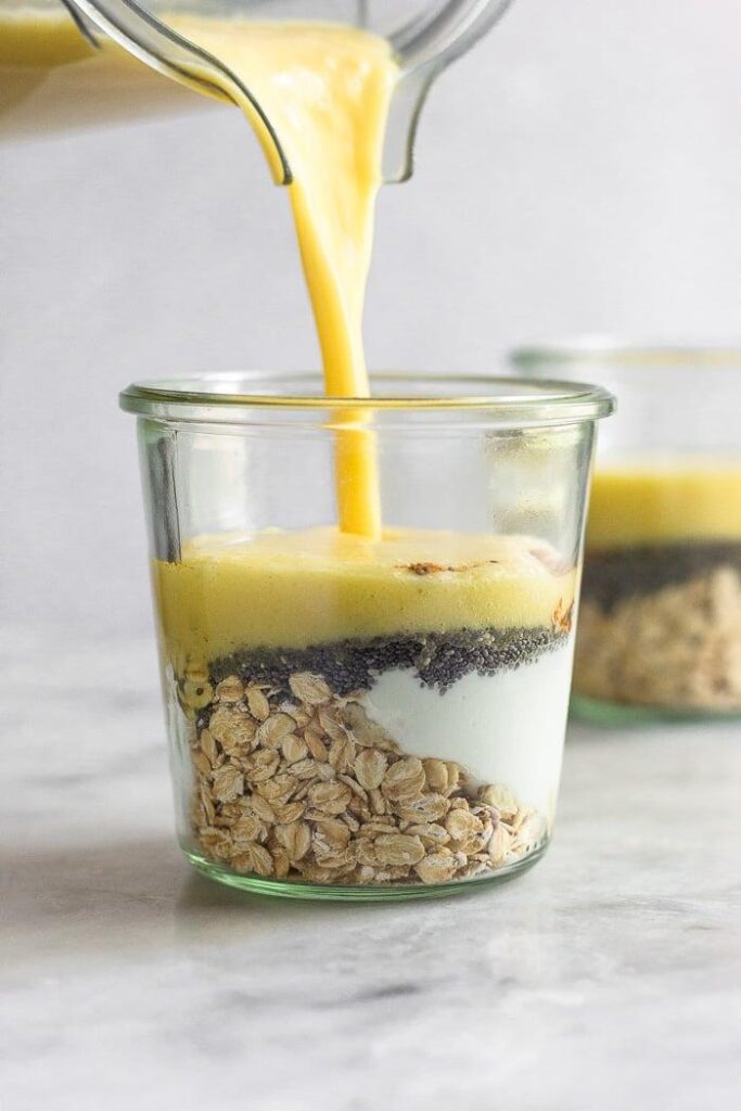 Tarro de cristal lleno de copos de avena, yogur griego y semillas de chía con un batido de leche de mango vertido en él.