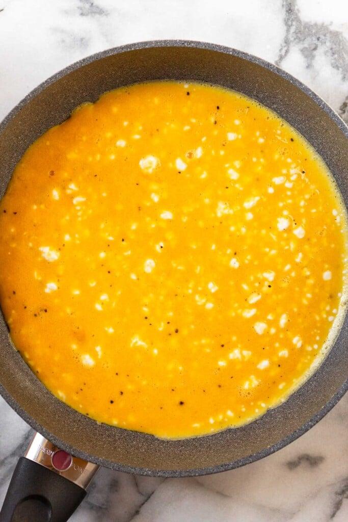 Toma aérea de una sartén grande con requesón en huevos revueltos esparcido por el fondo antes de que se cocinen.