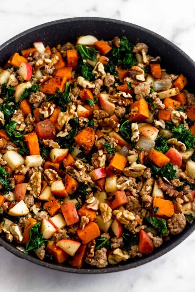 Gran sartén salteada con boniatos, salchichas, manzanas, col rizada, cebollas y nueces.